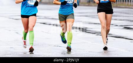 gruppo femminile corridori atleti maratona corsa, vista frontale donna gambe jogger in compressione calze correre strada bagnata Foto Stock