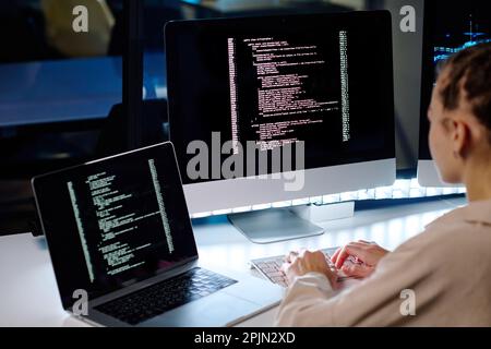 Concentratevi sullo schermo del computer con dati codificati mentre il tecnico IT è seduto alla scrivania di fronte al monitor in un ufficio buio e decodifica le informazioni Foto Stock