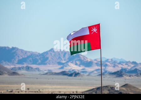 Bandiera dell'Oman che sventola sul vento nel deserto dell'Arabia Saudita con montagne sullo sfondo, al Ula, Arabia Saudita Foto Stock