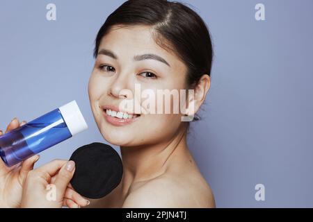 Ritratto di giovane donna asiatica con trucco e tampone di cotone nero su sfondo blu. Foto Stock