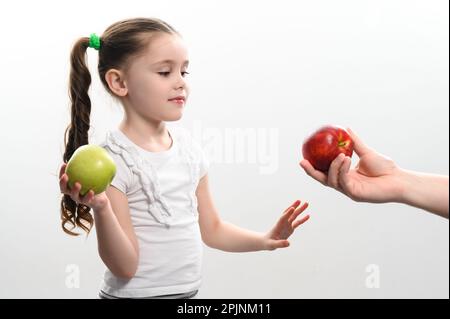 La bambina sceglie fra due mele, mela rossa o verde, scelta del bambino, sfondo bianco e spazio della copia. Foto Stock