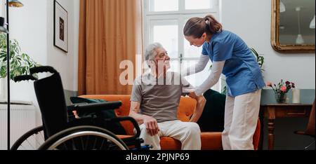Giovane infermiera che aiuta l'uomo anziano a alzarsi. Foto Stock