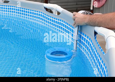 L'uomo pulisce lo skimmer per la piscina di telaio. Pulizia piscina contaminata. Foto Stock