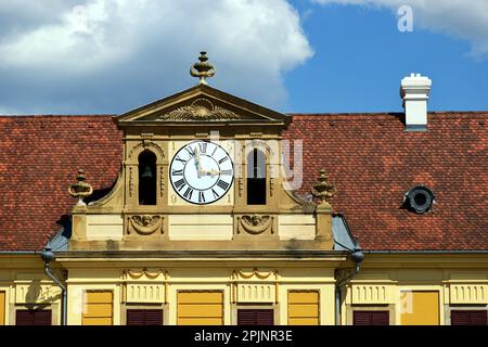 orologio rotondo bianco con pareti esterne decorative in mattoni gialli. numeri romani neri. tegole rosse di argilla tetto mansarda inclinato. bocca dormiente. architettura classica Foto Stock