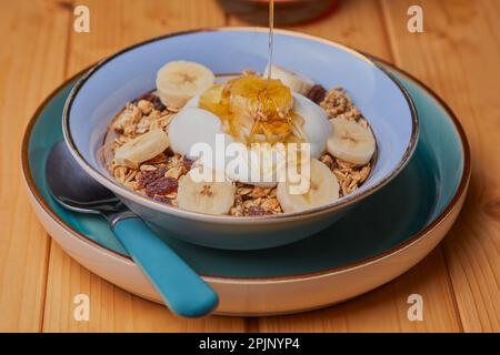 Ciotola di granola con yogurt a fette di banana e sgocciolato con miele. Foto Stock