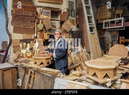 Fez, Marocco - 07 gennaio 2020: Uomo sconosciuto nella sua lavorazione del legno o scultura officina vicino al mercato di strada. molti souvenir di legno e prodotti intorno a lui Foto Stock