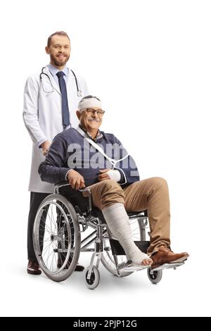 Uomo maturo con un braccio rotto e bendaggio sulla testa seduto su una sedia a rotelle e un medico in piedi dietro isolato su sfondo bianco Foto Stock
