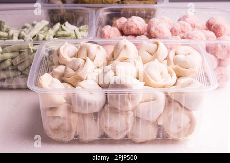 Ortaggi congelati e prodotti a base di carne semilavorati in contenitori di plastica su un piatto bianco. polpette, gnocchi, fagioli tritati Foto Stock