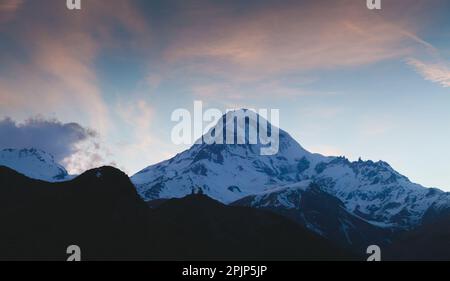 Monte Kazbek in serata. Georgiano paesaggio montano sotto colorato cielo notturno Foto Stock