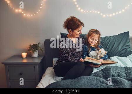 Mamma che legge libro sua figlia a letto prima di andare a dormire. Leggere storie prima di dormire. Storie di sonno per i bambini Foto Stock