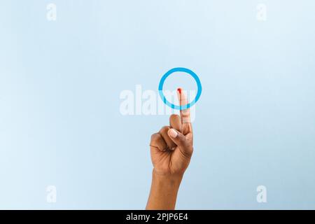 Mano di uomo biraciale con anello blu sopra dito sanguinante, su sfondo blu con spazio copia Foto Stock