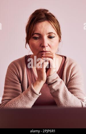 La donna si è concentrata sul suo lavoro lavorando sodo svolgendo il suo lavoro in remoto sul notebook da casa. Donna seduta alla scrivania di fronte al computer guardando lo schermo. Conce Foto Stock