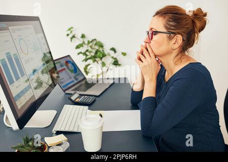 Imprenditrice donna si è concentrata sulla risoluzione del lavoro difficile. Donna d'affari confusa pensando duro tenere doccuments in piedi alla sua scrivania in ufficio Foto Stock