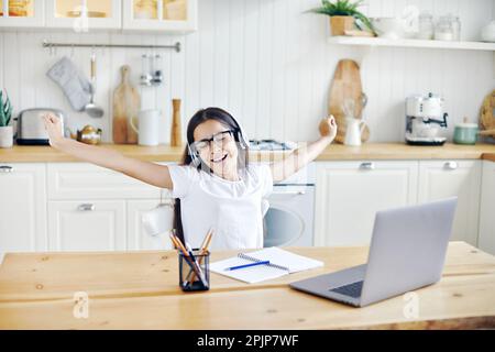 Bella pre-teen 12s ragazza in cuffie sedersi a tavolo con laptop finitura on-line classe, lezione con tutor, fare attività, prendere pausa, rilassarsi con le braccia r Foto Stock