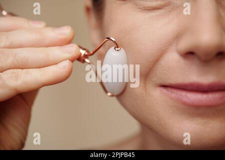 Immagine closeup di donna matura massaggiante viso con rullo di quarzo rosa Foto Stock