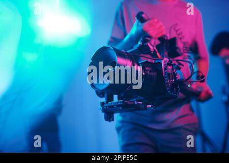 Primo piano delle riprese di un giovane cameraman con una fotocamera professionale mentre si eseguono contenuti in studio Foto Stock