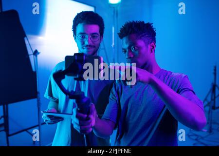 Il giovane operatore si trova su un cavalletto e discute con il regista di nuovi contenuti durante il lavoro in studio Foto Stock