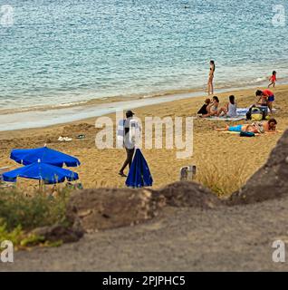 Nero, venditore di asciugamani maschio che mostra le sue merci a vacanzieri, Playa Blanca spiaggia. Febbraio 2023 Foto Stock