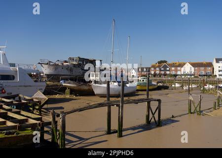 Un vecchio molo in legno in cattive condizioni sopra le fangose pianelle del fiume Arun a Littlehampton con vecchie barche sullo sfondo. Foto Stock