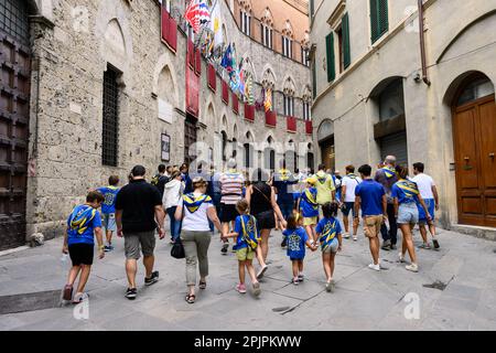 Siena, Italia - Agosto 15 2022: I membri della Tartuca o della Tartaruga Contrada camminano su Via di Città di fronte al Palazzo Chigi-Saracini Foto Stock