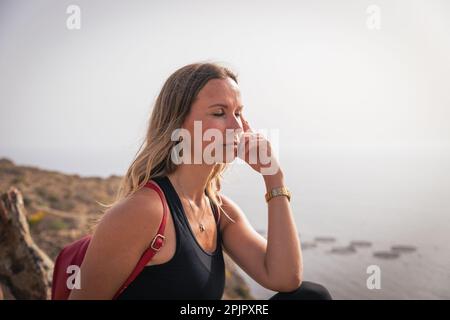 Una donna fa una pausa mentre si fa trekking e medita seduto su una roccia. Foto Stock