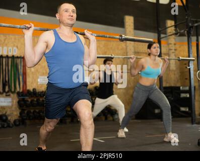 Bodybuilder maschile di mezza età che esegue esercizi di resistenza e resistenza durante il sollevamento di barbell di gruppo in classe CrossFit Foto Stock