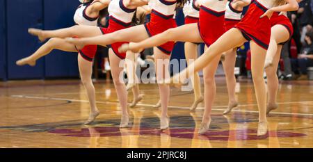 Le ragazze del kickline della scuola superiore che si esibiscono su un pavimento della palestra a metà tempo di una partita di basket. Foto Stock