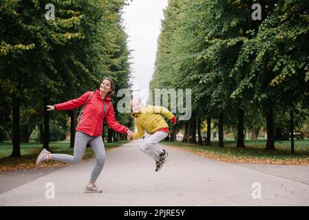 Madre e figlio saltano nel parco autunnale. Stagione autunnale. Felice giovane bella madre e suo figlio hanno una passeggiata nel parco Foto Stock