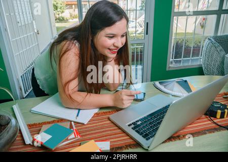 giovane donna ispanica latino interior designer sorridente in un incontro di affari online con un cliente che punta il portatile, discutendo l'incarico, worki Foto Stock