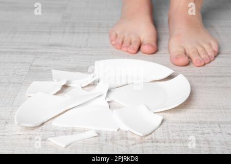 Donna a piedi nudi in piedi vicino al piatto rotto sul pavimento, primo piano Foto Stock