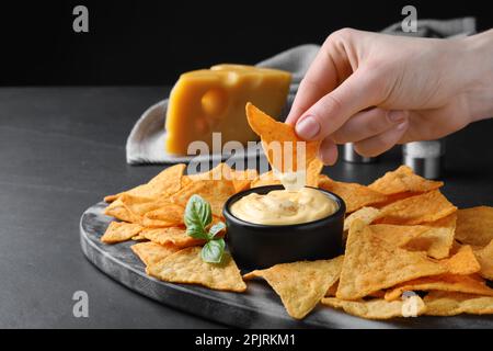 Donna che immerga nacho croccante in salsa di formaggio deliziosa a tavola nera, primo piano. Spazio per il testo Foto Stock