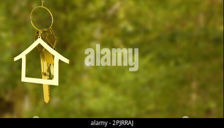 Immagine del modello della casa e della chiave appesa al campo erboso sfocato Foto Stock