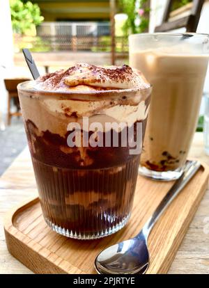 Due bicchieri di caffè ghiacciato; cioccolato e caffè alla vaniglia su un piatto di legno. Foto Stock