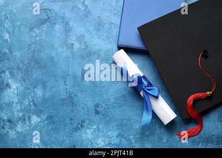 Diploma con nastro, cappello di laurea e libro su tavolo blu Foto Stock