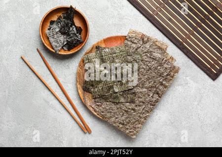 Piatto con fogli di nori, bacchette e tappeto di bambù su sfondo chiaro Foto Stock