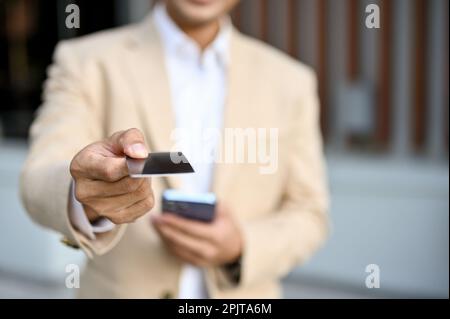 Primo piano immagine di un professionista millenario asiatico in un vestito da lavoro che consegna il suo biglietto da visita a una macchina fotografica. Foto Stock