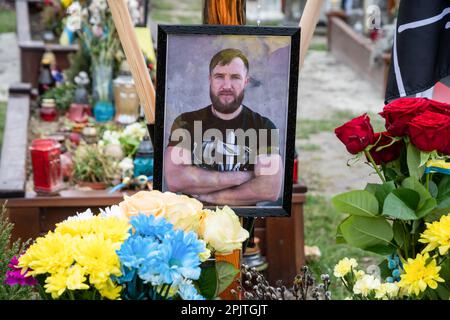 La tomba di un soldato caduto con un ritratto sul campo delle sepolture d'onore al cimitero di Lviv. Yurii Ruf era uno scrittore di Leopoli, figura pubblica, patriota dell'Ucraina e una persona ben nota a Leopoli e in Ucraina. Ha organizzato molti eventi, un festival, ecc. Quando iniziò la guerra, andò in prima linea come volontario e fu ucciso durante una missione di combattimento nella regione di Luhansk il 1 aprile 2022. L'evento nelle foto è la commemorazione di Yuriy nella chiesa e sul campo delle onorate sepolture nel cimitero di Lychakivskyi a Lviv nel primo anniversario della sua morte. Parenti, amici e residenti di Foto Stock