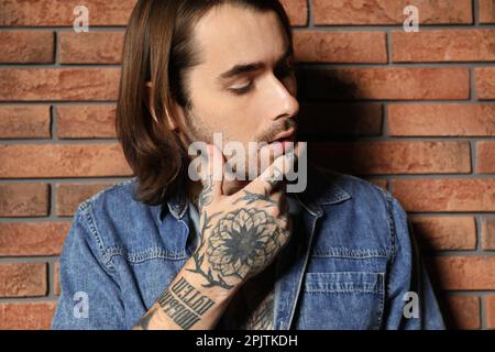 Giovane uomo con tatuaggi a portata di mano vicino al muro di mattoni Foto Stock