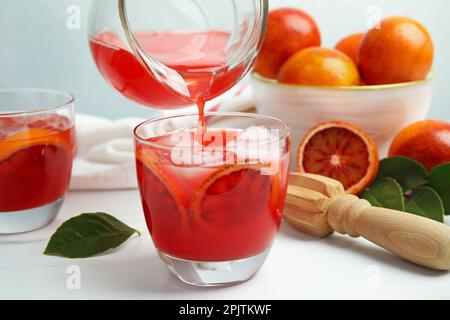 Versare un gustoso succo d'arancia siciliana nel bicchiere su un tavolo bianco Foto Stock