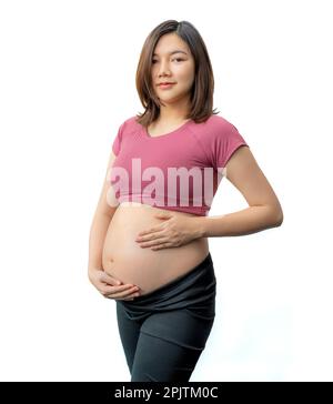 Donna incinta felice in abiti fitness in piedi tenendo la pancia esposta contro sfondo bianco, stanza per spazio copia Foto Stock