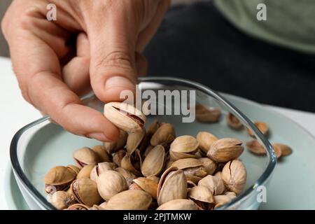 Donna che prende gustoso pistacchio arrosto dalla ciotola di vetro a tavola, primo piano Foto Stock