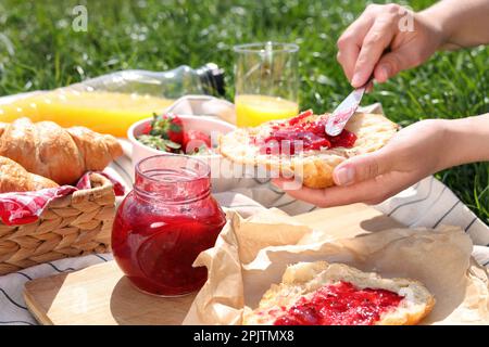 Donna che spalma marmellata su croissant all'aperto, primo piano. Picnic estivo Foto Stock