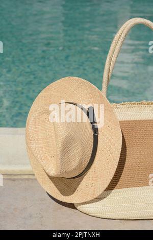 Elegante borsa e cappello vicino alla piscina all'aperto nelle giornate di sole. Accessori da spiaggia Foto Stock