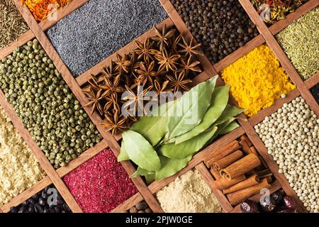 Spezie ed erbe per decorare le etichette dei prodotti alimentari . Stagionatura in scatola di legno come sfondo, vista dall'alto. Foto Stock