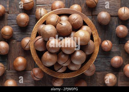 noci di macadamia sgusciate in ciotola su sfondo di tavolo di legno. Foto Stock