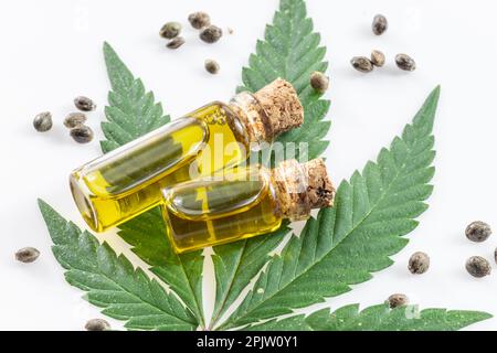 Foglie di cannabis e piccole bottiglie di olio di canapa isolate su sfondo bianco. Primo piano. Foto Stock