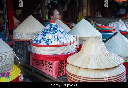 Una donna ride mentre si siede al suo stand vendendo tradizionali cappelli commerciali a PLEIKU Central Market, Vietnam. Foto Stock