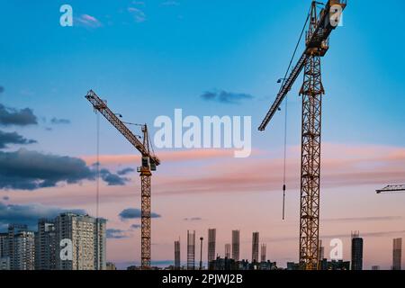 Grande cantiere con gru che lavorano su un complesso edilizio, con cielo tramonto Foto Stock