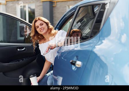 Seduti in auto. Giovane donna in abiti casual con la sua elettromobile all'aperto di giorno Foto Stock