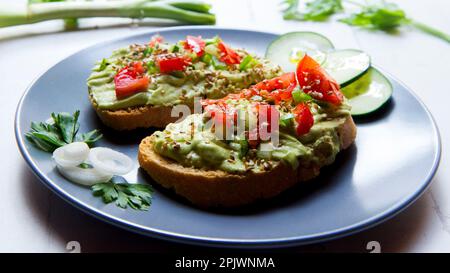 Due toast di pane biologico con avocado e pomodori ciliegini. Foto Stock